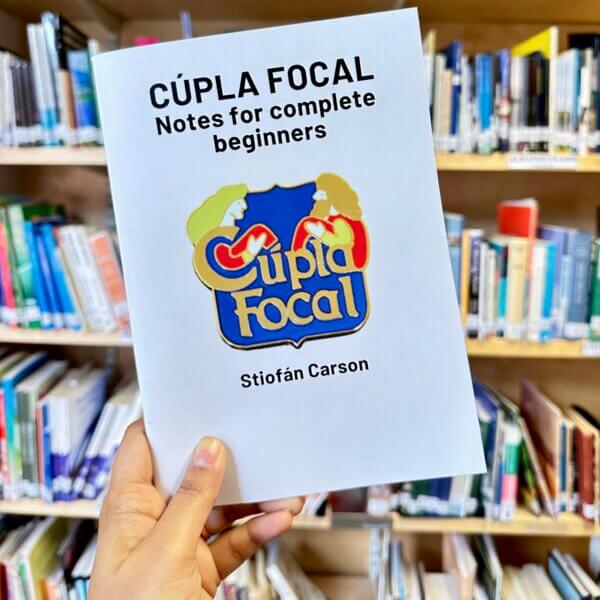 Cúpla Focal book by Stiofán Carson held up in front of book shelf